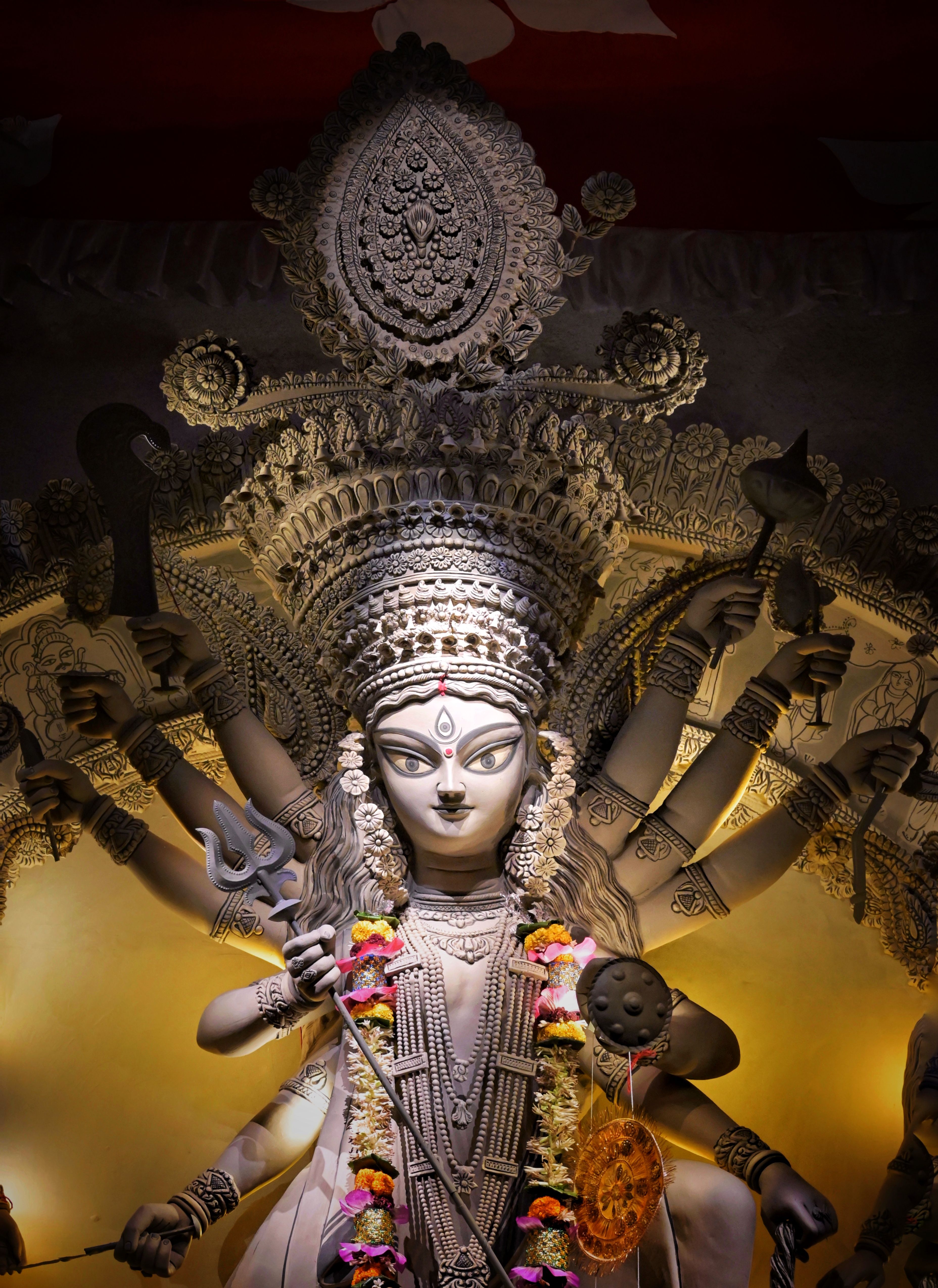 A grey stone-textured Durga idol lit against a golden teardrop halo — photo via Pexels / kolkatarchobiwala