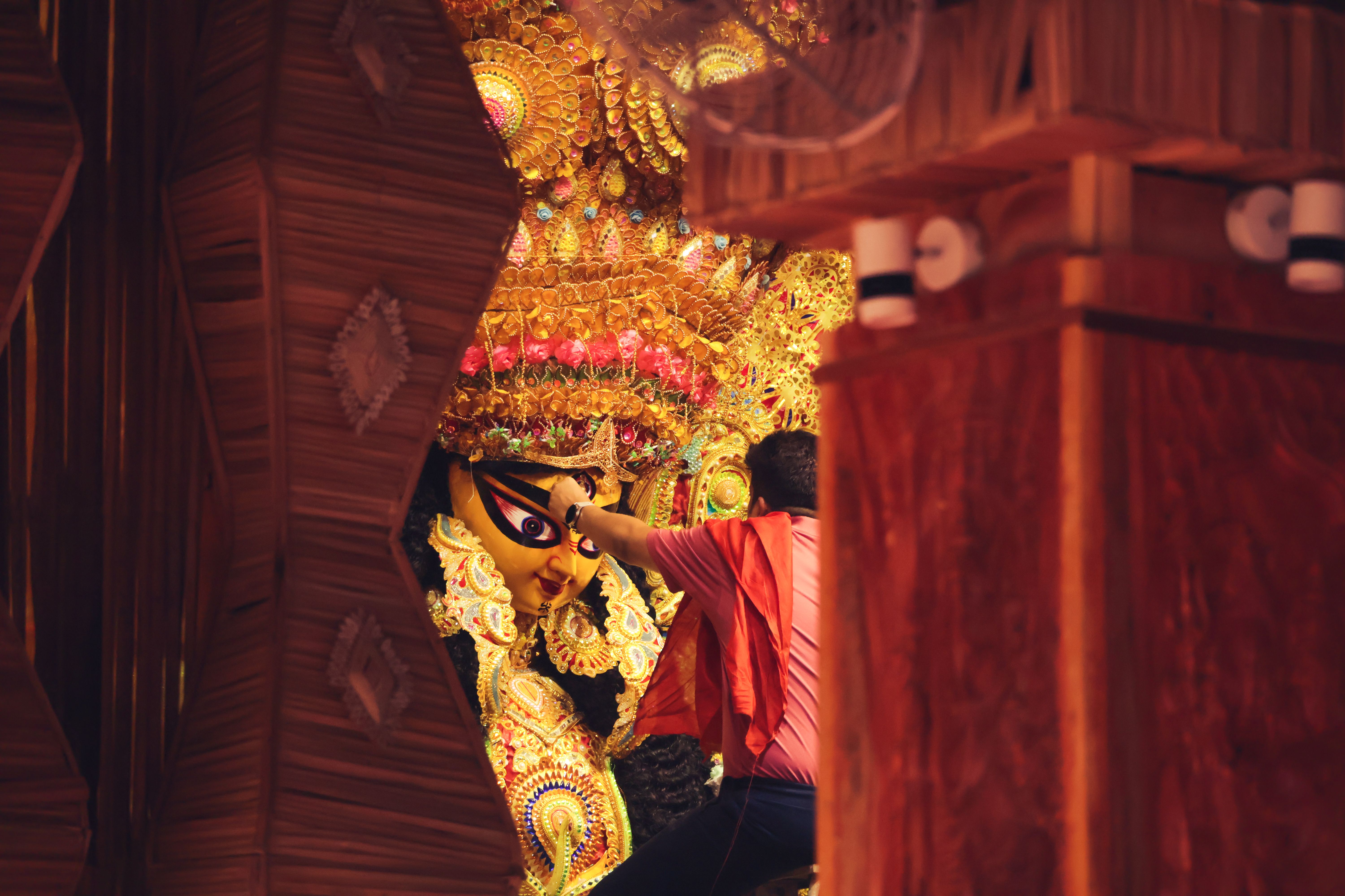 A volunteer adjusting the idol's crown, seen through a gap in the bamboo pandal wall — photo via Pexels / Sayak Mondal